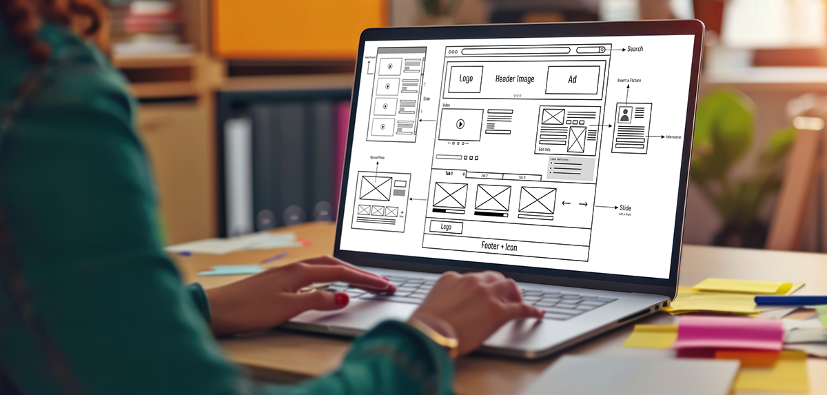 Student typing on laptop while viewing wireframes.