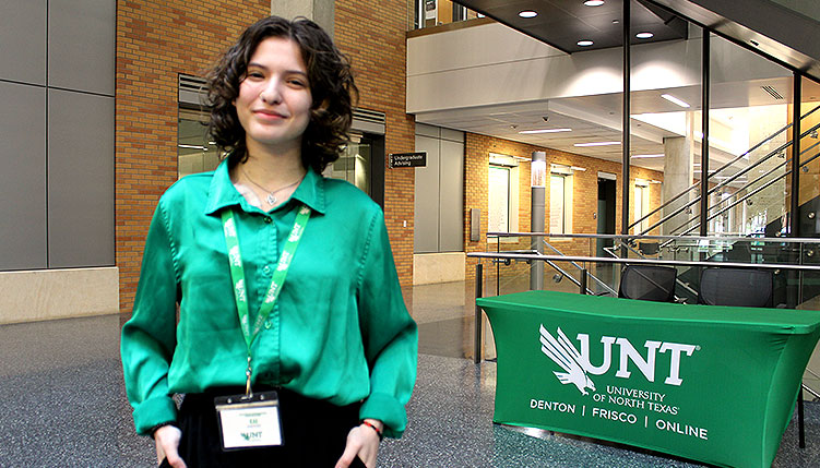 Student posing in front of welcome table and smiling at camera.